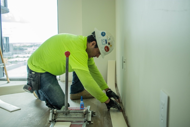 Man instaliing flooring wearing a yellow shirt